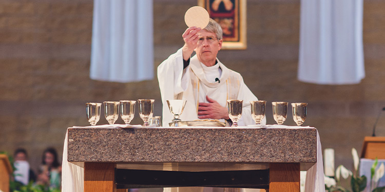 Pastor standing at chalice table holding up a wafer