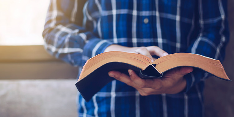 Closeup of man in a plaid, blue shirt holding an open bible