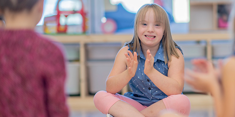 Young girl with down syndrome sits cross-legged, smiling